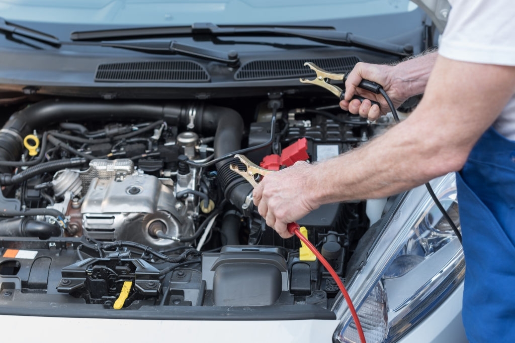 Car mechanic using cables to start a car engine